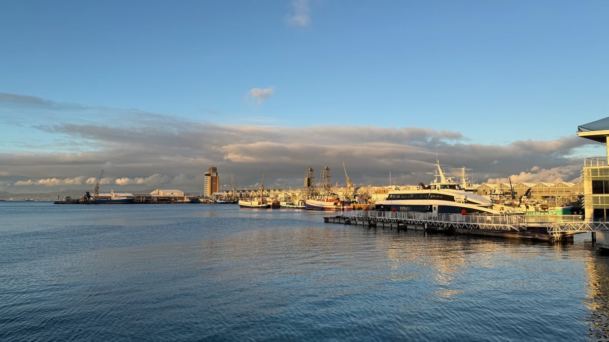 Scenic view of Cape Town harbor with boats at sunset, showcasing calm waters and serene sky.